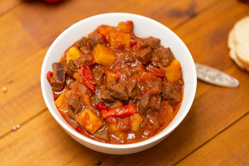Meat stew with beef, potato, carrot, onion, spices,tomato and pepper . Slow cooked meat stew, bowl, wooden background. Hot autumn-winter dish. Close up.