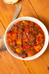 Meat stew with beef, potato, carrot, onion, spices,tomato and pepper . Slow cooked meat stew, bowl, wooden background. Hot autumn-winter dish. Close up.