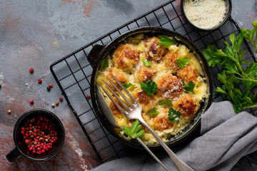 Meatballs with cheese and cream sauce in cast iron pan on gray vintage background. Top view.