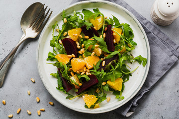 Beets, orange, pine nut, olive oil, feta cheese and arugula salad in ceramic plate on old concrete...