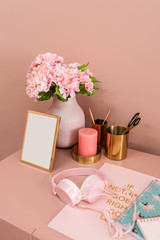 Working corner in pink color scheme with bouquet flower,gold vase,pink candle and golden frame on pink painted wall / cozy interior concept / fashion design / blogger
