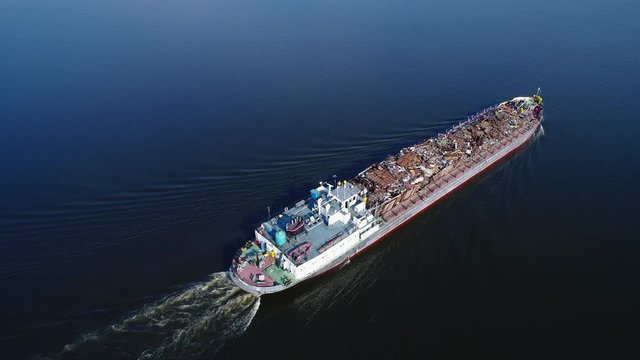Aerial view. A barge loaded with scrap metal and waste floating on a water surface. Transportation of recyclable materials by means of a dry cargo ship.
