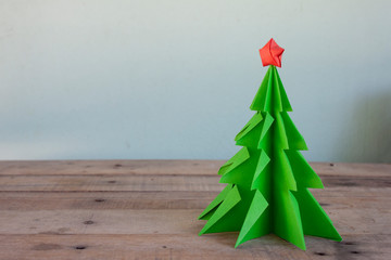 Concept origami the paper into christmas tree and red star on brown wooden table.