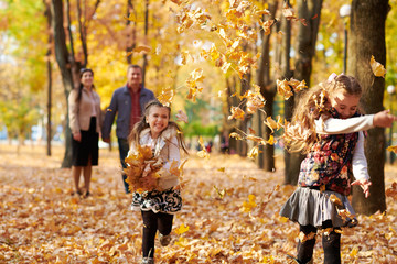 Happy family is in autumn city park. Children and parents running with leaves.. They posing, smiling, playing and having fun. Bright yellow trees.
