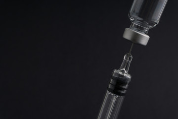 Medical syringe and vial on dark background with selective focus and crop fragment