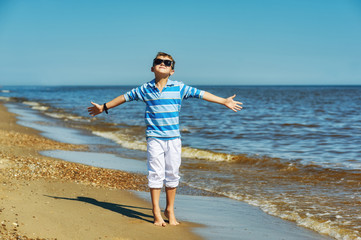 A boy on a walk along the sea coast . Child in white trousers and t-shirt