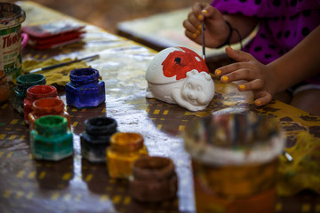 Creative items and crafts for children at home on the table. Paints and brushes, scissors, thread and scraps of fabric - the hands of the child and the parent in the background.