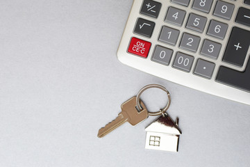 Calculator and key with house shape pendant on silver color background with copy space for text. Real estate purchase or apartment rent planning concept.