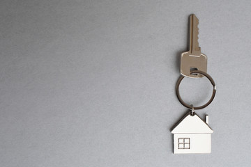 Fototapeta na wymiar Key with metal house shaped pendant on grey background closeup view with copy space for text. Real estate, buying and moving new home or renting property concept.