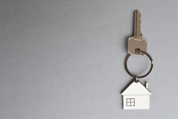 Key with metal house shaped pendant on grey background closeup view with copy space for text. Real...