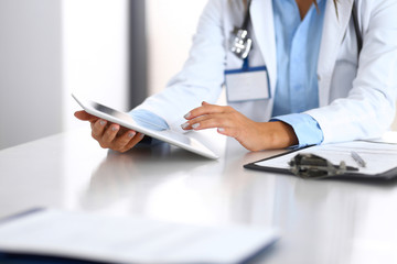 Unknown doctor woman using tablet computer while standing straight near window in hospital, close-up of hands. Medicine and health care concept