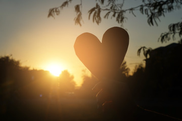 Young woman holding decorative heart outdoors at sunset