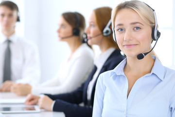 Call center. Group of operators at work. Focus at blonde business woman in headset