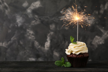 Tasty chocolate cupcake with sparkler on wooden table against grunge background
