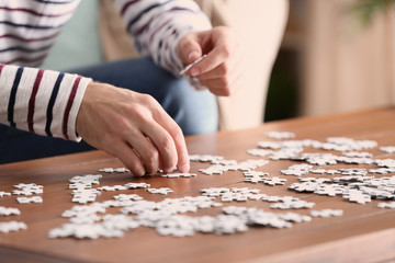 Fototapeta na wymiar Young man doing jigsaw puzzle at home, closeup