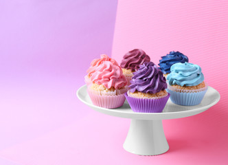 Stand with tasty cupcakes on color background