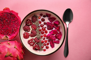 Yogurt with berries and cut dragon fruit in bowl on color background