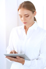 Beautiful blonde businesswoman using tablet pc while standing straight in a brightly lit office. Business concept