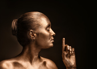 Beautiful young woman with golden paint on her body against dark background