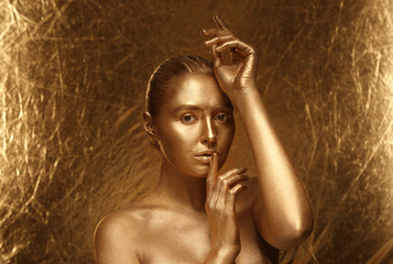 Beautiful young woman with golden paint on her body against shiny color background