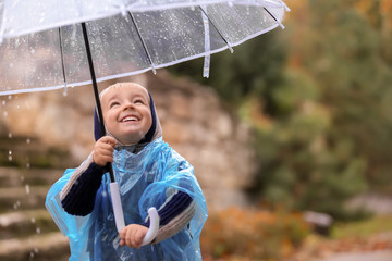 Cute little boy with transparent umbrella under rain outdoors