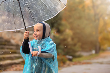 Cute little boy with transparent umbrella under rain outdoors