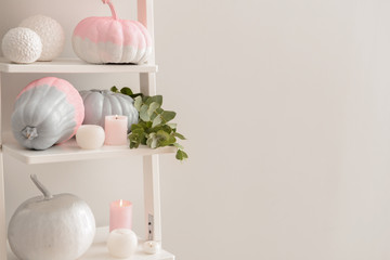Painted pumpkins with burning candles on shelving near light wall