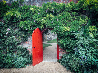 Fototapeta na wymiar Open red door in a brick wall with winding path behind