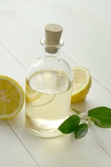 Lemon essential oil in a glass bottle  fresh lemon in cut with green leaves on a white wooden board background