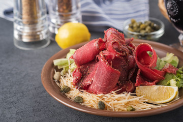 Raw frozen meat stroganina with cheese, capers and lemon. Sliced frozen raw meat on a plate. Cold snack  with copyspace
