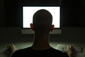 Hacker committing crime on a desktop computer in the dark.