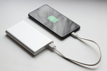 A modern smartphone is charging from a power bank. 100% charge. On a light background..