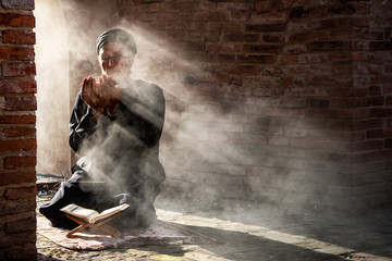 Silhouette of muslim male praying in old mosque with lighting and smoke background