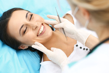 Obraz na płótnie Canvas Young female patient visiting dentist office.Beautiful woman with healthy straight white teeth sitting at dental chair with open mouth during oral checkup while doctor working at teeth