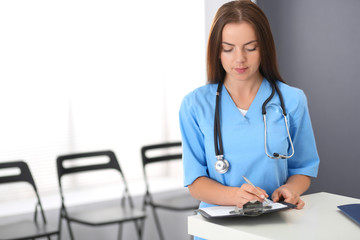 Doctor woman at work. Portrait of female physician filling up medical form while standing near reception desk at clinic or emergency hospital. Medicine and healthcare concept