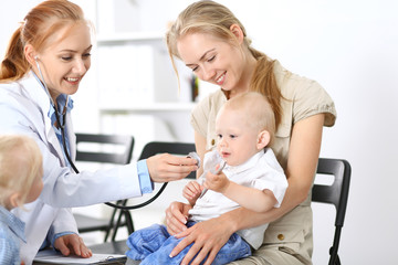 Doctor examining a little boy with stethoscope. Mother holds her son on her lap. Motherless and medicine concept