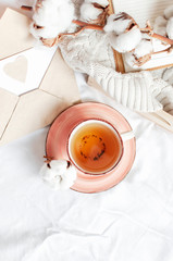 Cup of hot tea branch of cotton wooden tray knitted plaid sweater open notebook love letter in bed. Cozy morning breakfast at home. Lifestyle gentle background Copy Space autumn winter concept