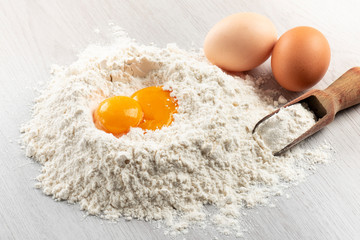 pile of flour with egg yolks for dough on table