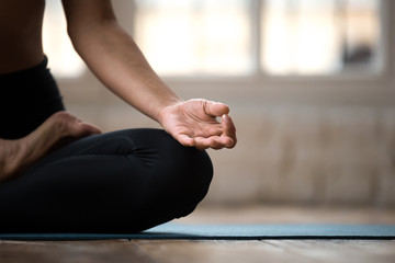 Young sporty yogi woman practicing yoga, doing Ardha Padmasana exercise, Half Lotus pose with mudra...