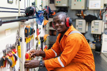 African marine engineer officer in engine control room ECR. He works in workshop and chooses correct tools and equipment