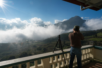 Fototapeta na wymiar Male tourist taking photo of mountain landscape with low white clouds under brilliant sky. Ideas for travel and tourism.