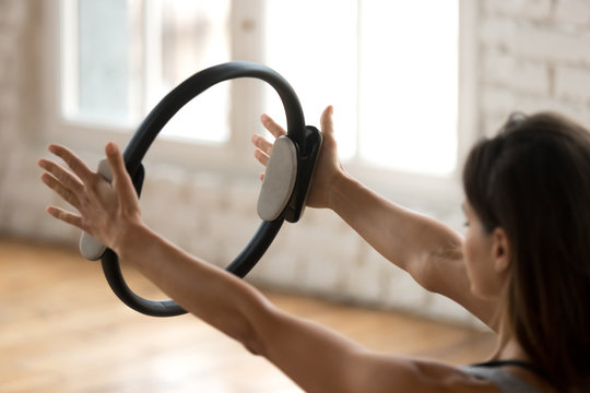 Young sporty attractive woman doing pilates toning exercise for arms and shoulders with ring, fitness with pilates magic circle in hands, working out, indoor close up. Strength, well being concept