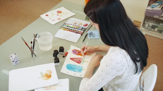 Young woman artist drawing watercolor paints and looked into the camera.