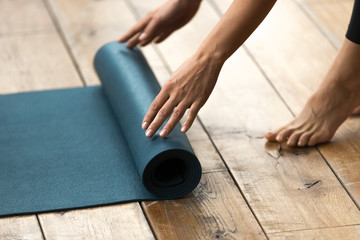 Fit beautiful woman folding blue exercise mat on wooden floor before or after working out in yoga studio club or at home Top close up view. Equipment for fitness, pilates or yoga, well being concept - obrazy, fototapety, plakaty