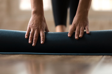 Front close up view of female hands rolling blue exercise mat on the floor before beginning her training session in yoga studio club at home. Equipment for fitness, pilates, yoga, well being concept