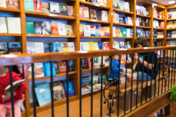 Blurred abstract background of bookshelves in book store, with a girl reading book in the store.