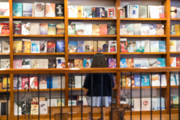 Blurred abstract background of bookshelves in book store, with a girl reading book in the store.