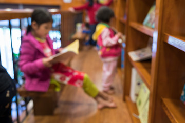 Blurred abstract background of bookshelves in book store, with children reading book in the store.