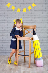 Cute school girl posing in studio shoot in school uniform dress and jacket on background of letters...
