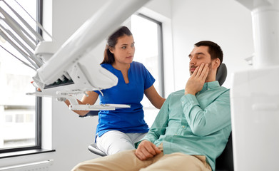 Fototapeta premium medicine, dentistry and healthcare concept - female dentist and male patient suffering from toothache at dental clinic